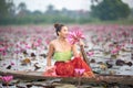 Young Asian women in Traditional dress in the boat and pink lotus flowers in the pond.