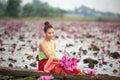 Young Asian women in Traditional dress in the boat and pink lotus flowers in the pond.
