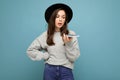 young asking dissatisfied brunette woman speaking wearing black hat and grey sweater holding smartphone looking to the