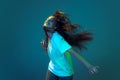 Young astonished girl with long loose hair dancing isolated on blue background in neon light. Concept of beauty, art