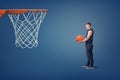 A young athlete with a basketball ball in his hands stands near an orange hoop. Royalty Free Stock Photo