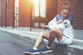 Young athlete in blue windrunner sitting on the street adjusting running program for his morning workout using mobile phone in Royalty Free Stock Photo