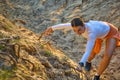 Young athlete climbs up the rough terrain clinging to the roots of trees with her hands.