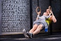 Young athlete father and little cute son exercising with gimnastic rings and smiling against brick wall in the gym.