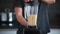 Young athlete man mixing hummus in a modern grey kitchen. Preparation of chickpea spread hommos in blender. Lentil dip, with spice