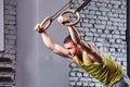 Young athlete man in the sportwear pulling up on gymnastic rings against brick wall in the cross fit gym. Royalty Free Stock Photo