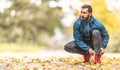 A young athlete in warm sportswear ties his shoelaces while running in an autumn park