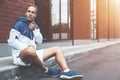 Young athlete in windrunner sitting on the street after good jogging session Royalty Free Stock Photo