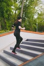 Young athletic beautiful brunette girl in black uniform, cap with headphones doing sport exercises, training and running Royalty Free Stock Photo