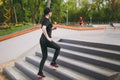 Young athletic beautiful brunette girl in black uniform, cap with headphones doing sport exercises, training and running Royalty Free Stock Photo