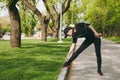 Young athletic beautiful brunette girl in black uniform and cap with headphones doing sport stretching exercises, warm Royalty Free Stock Photo