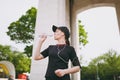 Young athletic beautiful brunette girl in black uniform, cap with headphones holding bottle drinking water during Royalty Free Stock Photo