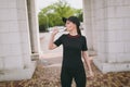 Young athletic beautiful brunette girl in black uniform and cap holding bottle, drinking water during training before Royalty Free Stock Photo