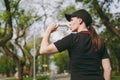 Young athletic beautiful brunette girl in black uniform and cap holding bottle, drinking water during training before Royalty Free Stock Photo