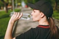 Young athletic beautiful brunette girl in black uniform and cap holding bottle, drinking water during training before Royalty Free Stock Photo