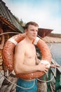 This is a young athletic guy in shorts and bare-chested standing with an old lifebuoy.