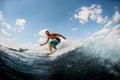 Athletic guy wakesurfer actively ride on the waves on surfboard against blue sky