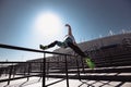 Young athletic man dressed in the white t-shirt, black leggings and blue shorts is jumping over the railing on the