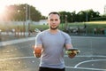 Young athletic man in a t-shirt holds a Burger and an Apple in the background of the stadium, a choice of healthy and Royalty Free Stock Photo