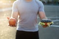 Young athletic man in a t-shirt holds a Burger and an Apple in the background of the stadium Royalty Free Stock Photo