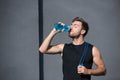 Young athletic man in tanktop holding a jumping rope and drinking water from