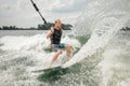Young athletic man wakesurfing on the board holding a cable