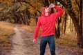 young athletic runner in a red sports jacket with a hood and black sport leggins quickly drink water