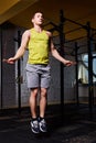 Young athletic sportsman in the sportwear working with jumping rope in cross fit gym against brick wall.