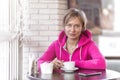 A young athletic trainer in a purple hoodie sits in a cafe and drinks coffee from a white cup. Daytime, lunch