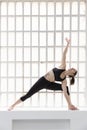 Young athletic woman in black sportswear practicing yoga next to a big window in her studio