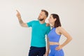 Young athletic woman and man in blue sportswear standing and pointing by finger, white background. Keeping fit by Royalty Free Stock Photo