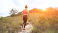 Young athletic woman running on mountain trail. Sunset Workout in Nature. Fit girl in pink top run.