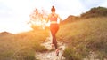 Young athletic woman running on mountain trail. Sunset Workout in Nature. Fit girl in pink top run.