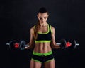 Young athletic woman in sportswear with dumbbells in studio against black background. Ideal female sports figure. Royalty Free Stock Photo