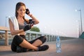 Young athletic woman using phone while siting on sidewalk and resting after running over the bridge. Royalty Free Stock Photo