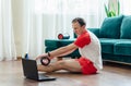 A young athleticman in red shorts is doing exercises on a foam roller using notebook laptop. Works out of the muscles Royalty Free Stock Photo