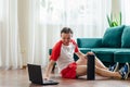 A young athleticman in red shorts is doing exercises on a foam roller using notebook laptop. Works out of the muscles Royalty Free Stock Photo