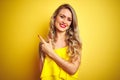 Young attactive woman wearing t-shirt standing over yellow isolated background cheerful with a smile of face pointing with hand Royalty Free Stock Photo