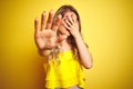 Young attactive woman wearing t-shirt standing over yellow isolated background covering eyes with hands and doing stop gesture