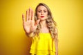 Young attactive woman wearing t-shirt standing over yellow isolated background doing stop sing with palm of the hand