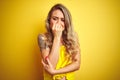 Young attactive woman wearing t-shirt standing over yellow isolated background looking stressed and nervous with hands on mouth Royalty Free Stock Photo