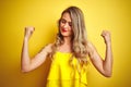 Young attactive woman wearing t-shirt standing over yellow isolated background showing arms muscles smiling proud