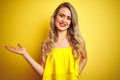 Young attactive woman wearing t-shirt standing over yellow isolated background smiling cheerful presenting and pointing with palm Royalty Free Stock Photo