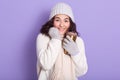 Young attarctive woman basking her hands via cup of hot beverage and gloves, wearing sweater, scarf and cap, posing isolated over Royalty Free Stock Photo