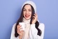 Young attarctive woman holding cap ofhot beverage in her hands, wearing white warm sweater, scarf and cap, posing isolated over