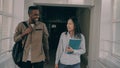 Young attractive african american male and asian female students are moving down corridor discussing something Royalty Free Stock Photo