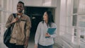 Young attractive african american male and asian female students are moving down corridor discussing something Royalty Free Stock Photo