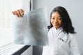 Young attractive african female doctor radiologist looking at x-ray image, while standing in light modern office in Royalty Free Stock Photo