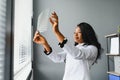 Young attractive african female doctor radiologist looking at x-ray image, while standing in light modern office in Royalty Free Stock Photo