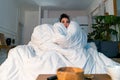 Young attractive anxious woman watching TV series and wrapping in big white blanket. cold autumn or winter time spending